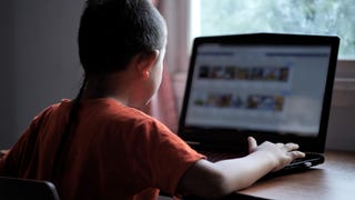 A child with their back to the camera uses a laptop.